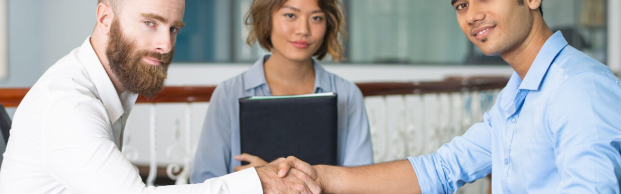 Content Indian candidate shaking hands with company leader at and of job interview. Asian HR manager posing in background. Job interview concept